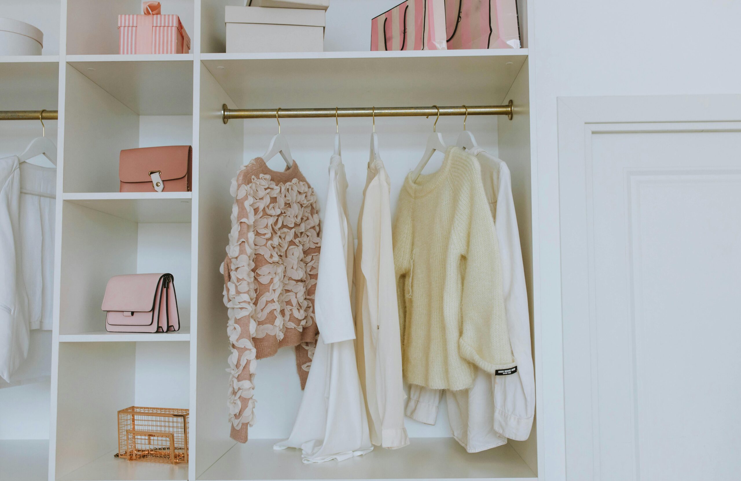 A neat, well-organized closet showcasing white and pink clothes and accessories on velvet hangers — a chic, clean wardrobe setup.