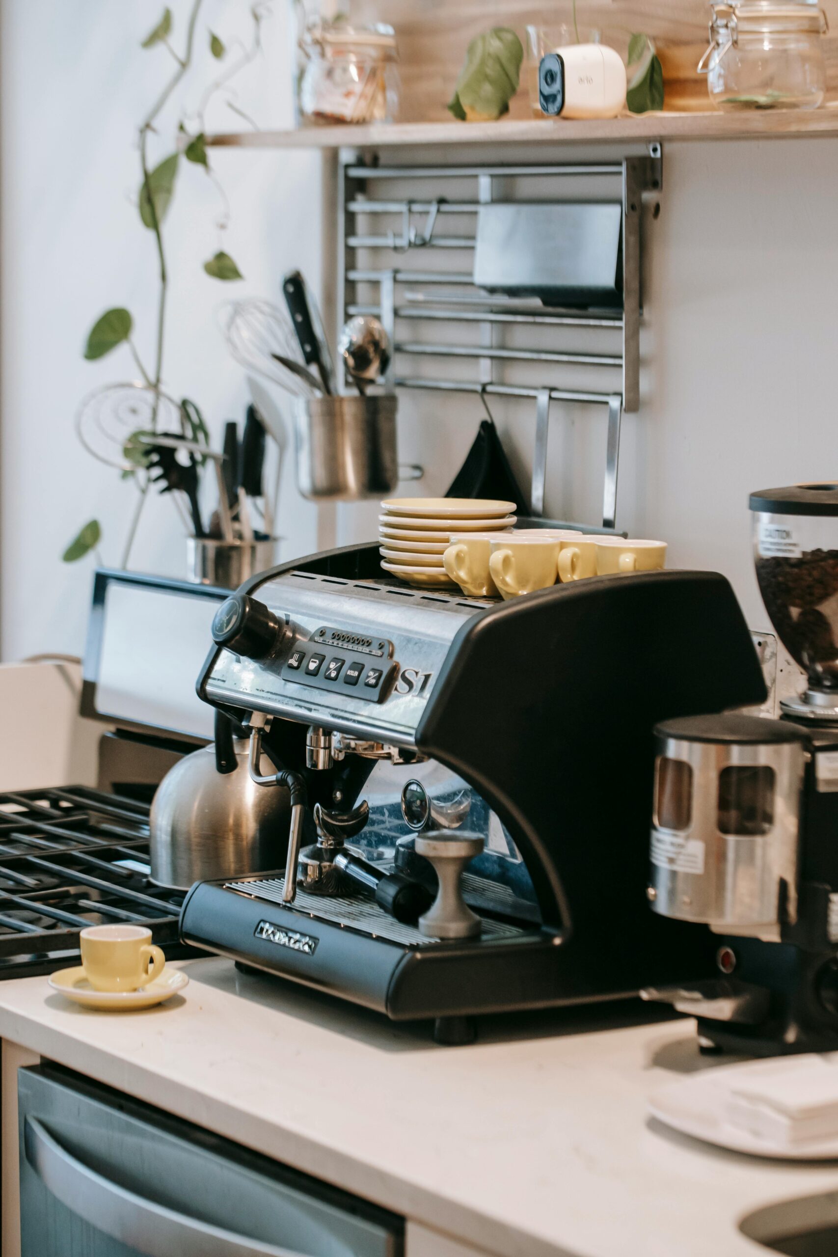 A small kitchen coffee bar setup with espresso maker, ceramic cups on open shelves, and a clean countertop — a cozy home coffee station.