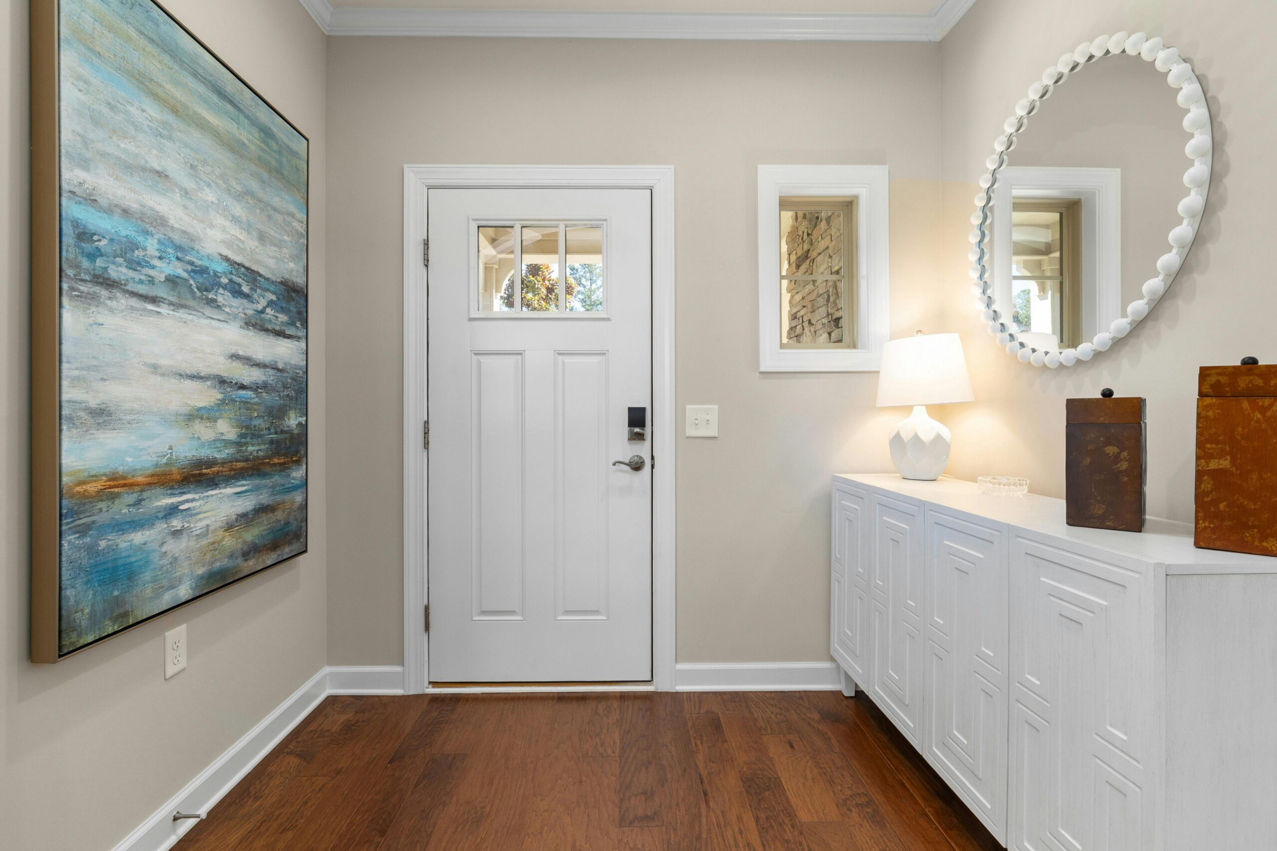 A bright and modern entryway with white walls, a clean console, abstract art, and elegant decor — small space organization inspiration.